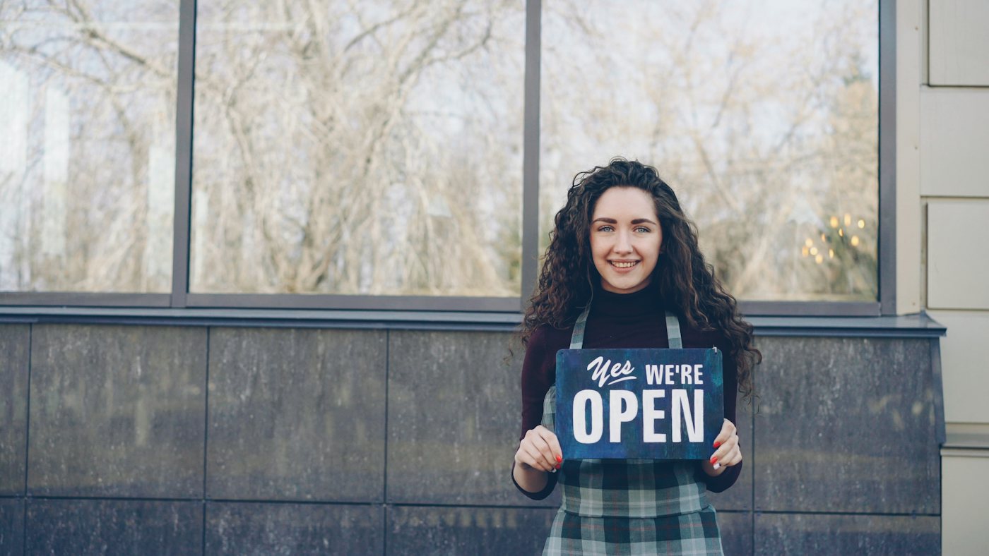 Shop owner holding an Open sign at her front door